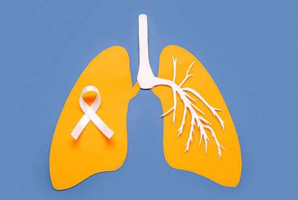 Yellow paper cutout of human lungs with a white lung cancer awareness ribbon on a blue background.